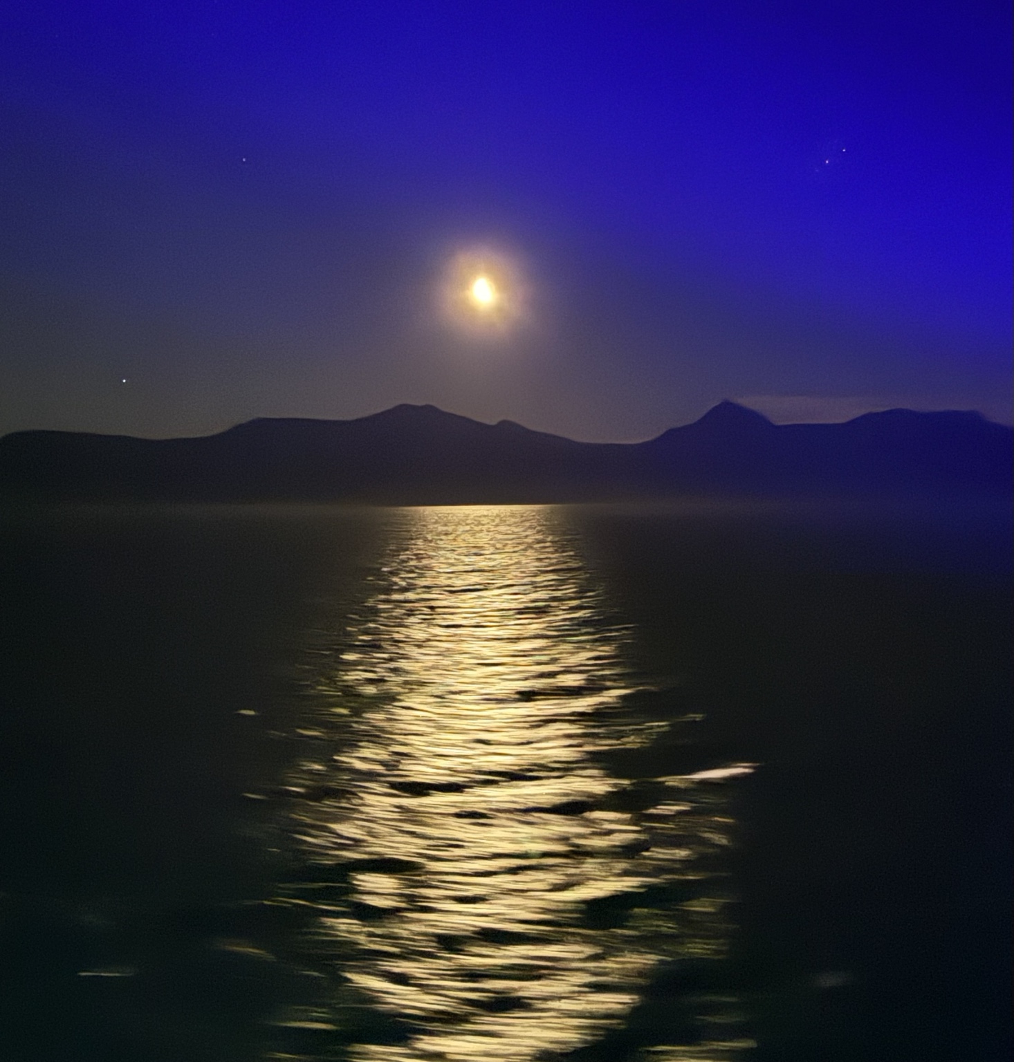 Moonlight reflected on dark water with mountains on the horizon